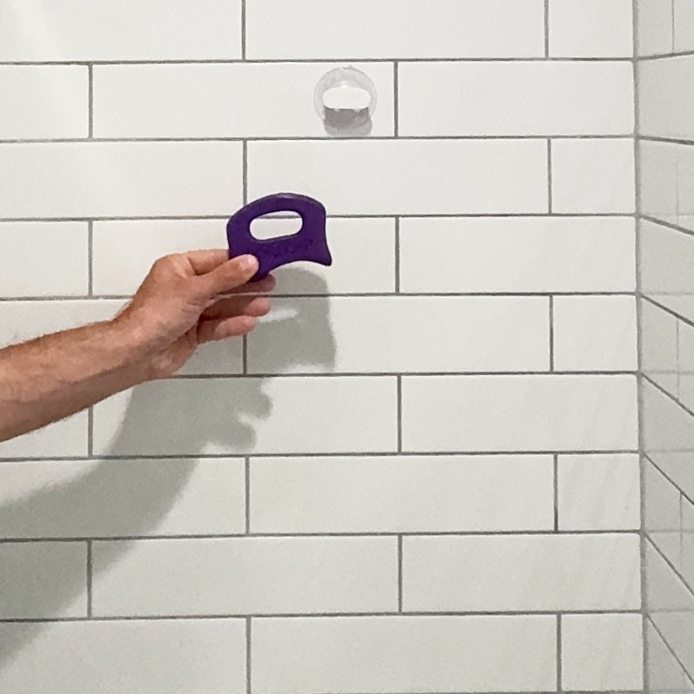 Hand holding a purple tool against a tiled wall